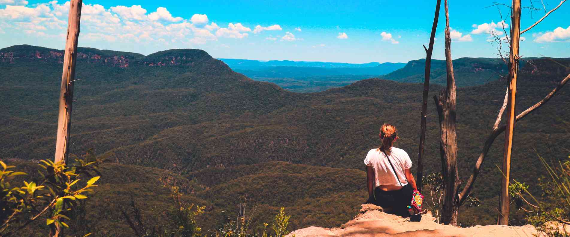 woman sitting on cliff looking out at mountain range